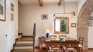 A dining area with a wooden table and chairs, a lamp, and a window with a view of greenery. -  Il Mulino Di Vogognano by Geco Vacation Rentals (Subbiano)