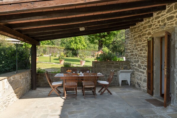 Une terrasse extérieure avec une table en pierre et des chaises en bois, un mur en pierre et une vue sur un jardin.