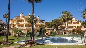 Et hotel med flere balkoner, en swimmingpool og palmer.