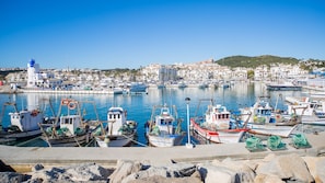 A marina with boats docked, a lighthouse, and a coastal town in the background.