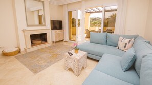 A living room with a sofa, a TV, a fireplace, and a view through a glass door.