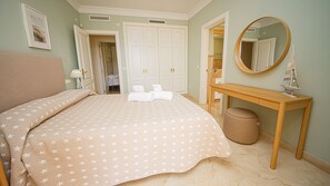 A bedroom with a bed, bedside tables, a mirror, and a door leading to another room.