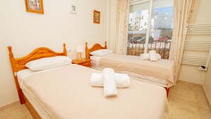 A hotel room with two beds, a window with a view of parked cars, and a radiator. - Terrazas de los Hidalgos F21A (Manilva)