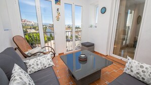 A balcony with a wicker sofa, a glass table, and a view of the cityscape. - Terrazas de los Hidalgos F21A (Manilva)