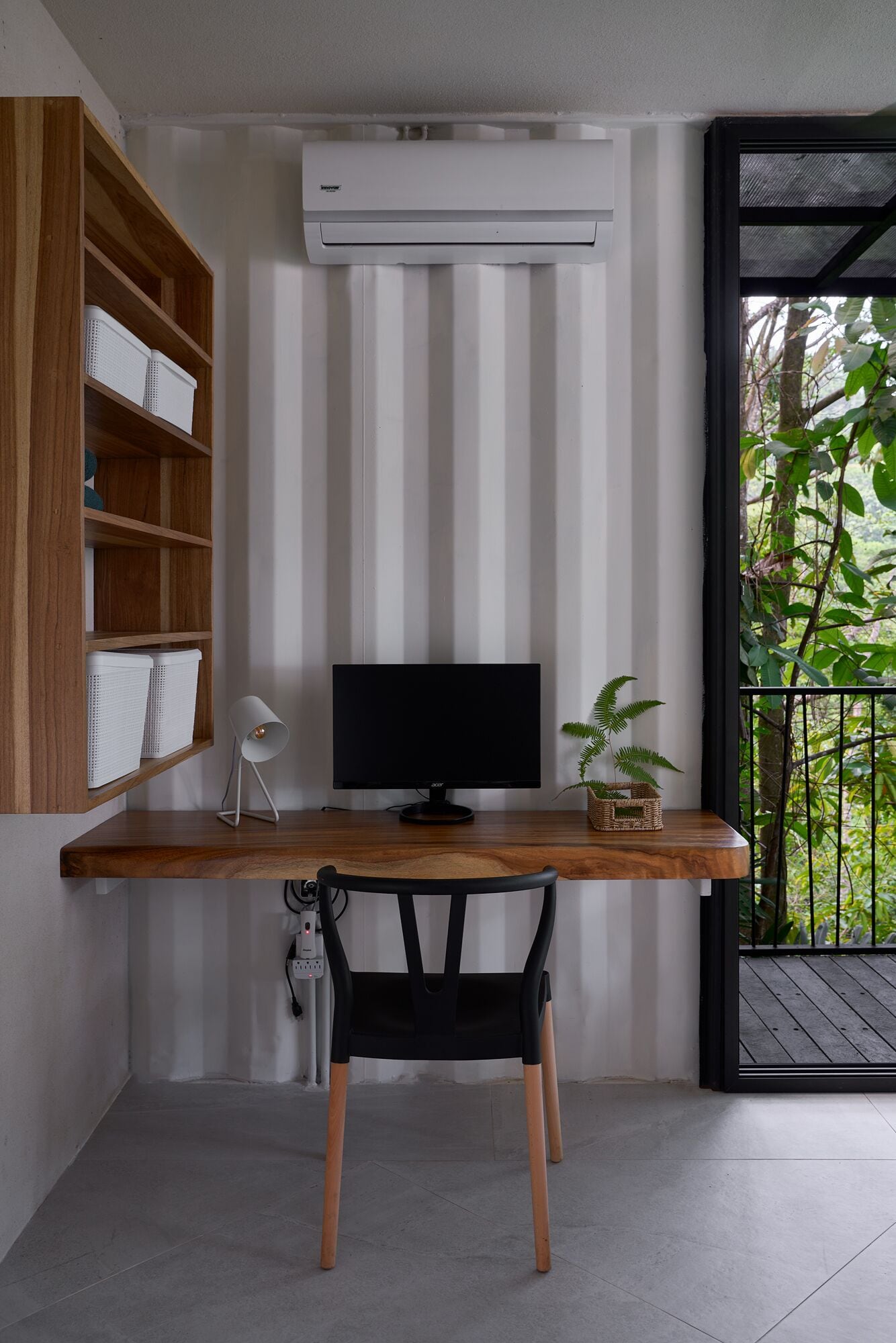 A modern workspace with a wooden desk, a black chair, a flat-screen monitor, and a white lamp.