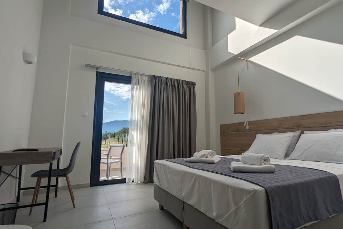 A modern hotel room with a large bed, a desk, and a view of the outdoors.
