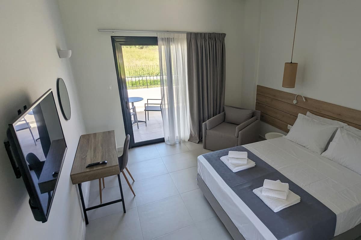 A hotel room with a bed, a desk, a chair, a TV, and a view of the outdoors.