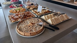 Een buffet met diverse gerechten, waaronder gebak, belegde broodjes en een groot stuk taart.