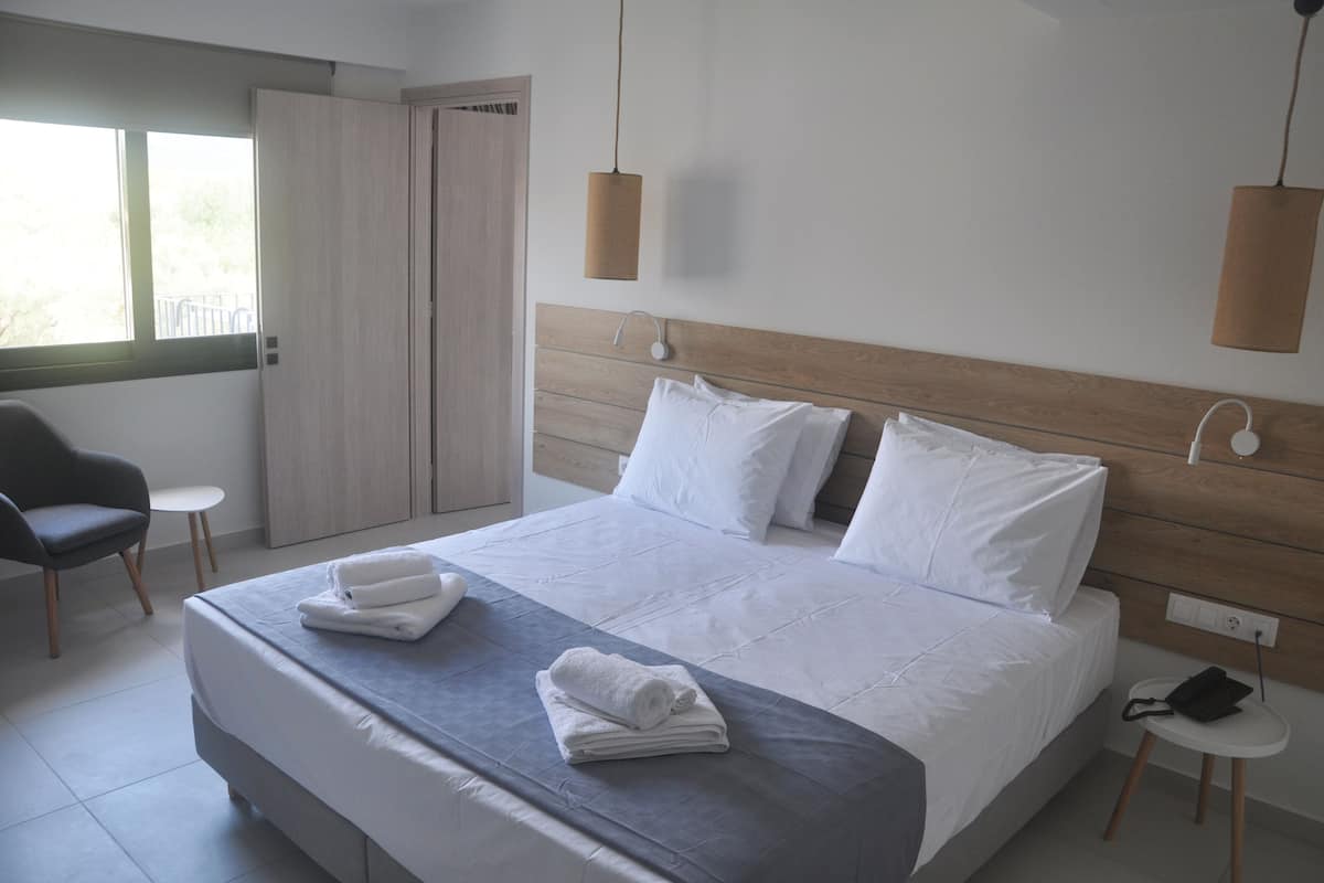 A modern hotel room with a large bed, a chair, a small table, and a wardrobe.