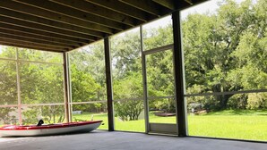 Amplia habitación con grandes ventanales que dan a un espacio verde y árboles. Se puede ver una embarcación en el lado izquierdo de la habitación.