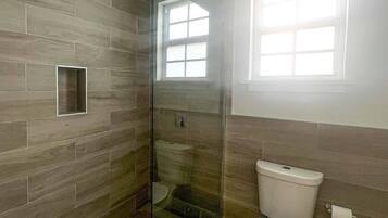 A bathroom with a glass-enclosed shower, a toilet, and a window providing natural light.
