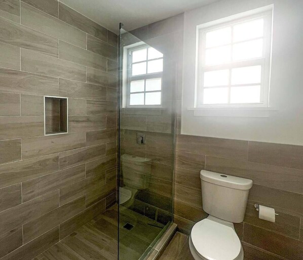 Un baño con ducha de mampara de vidrio, inodoro y ventana que proporciona luz natural.