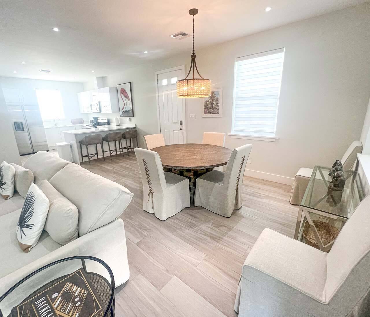 A modern living room with a round dining table, light-colored sofas, and a glass coffee table.