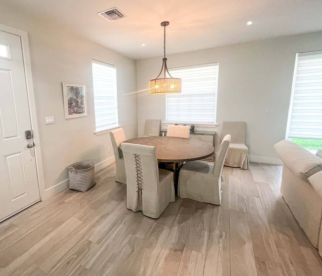 A dining area with a round table, six chairs, and a hanging light fixture.
