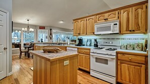Una cocina con armarios de madera, microondas, estufa y un comedor con lámpara de araña.