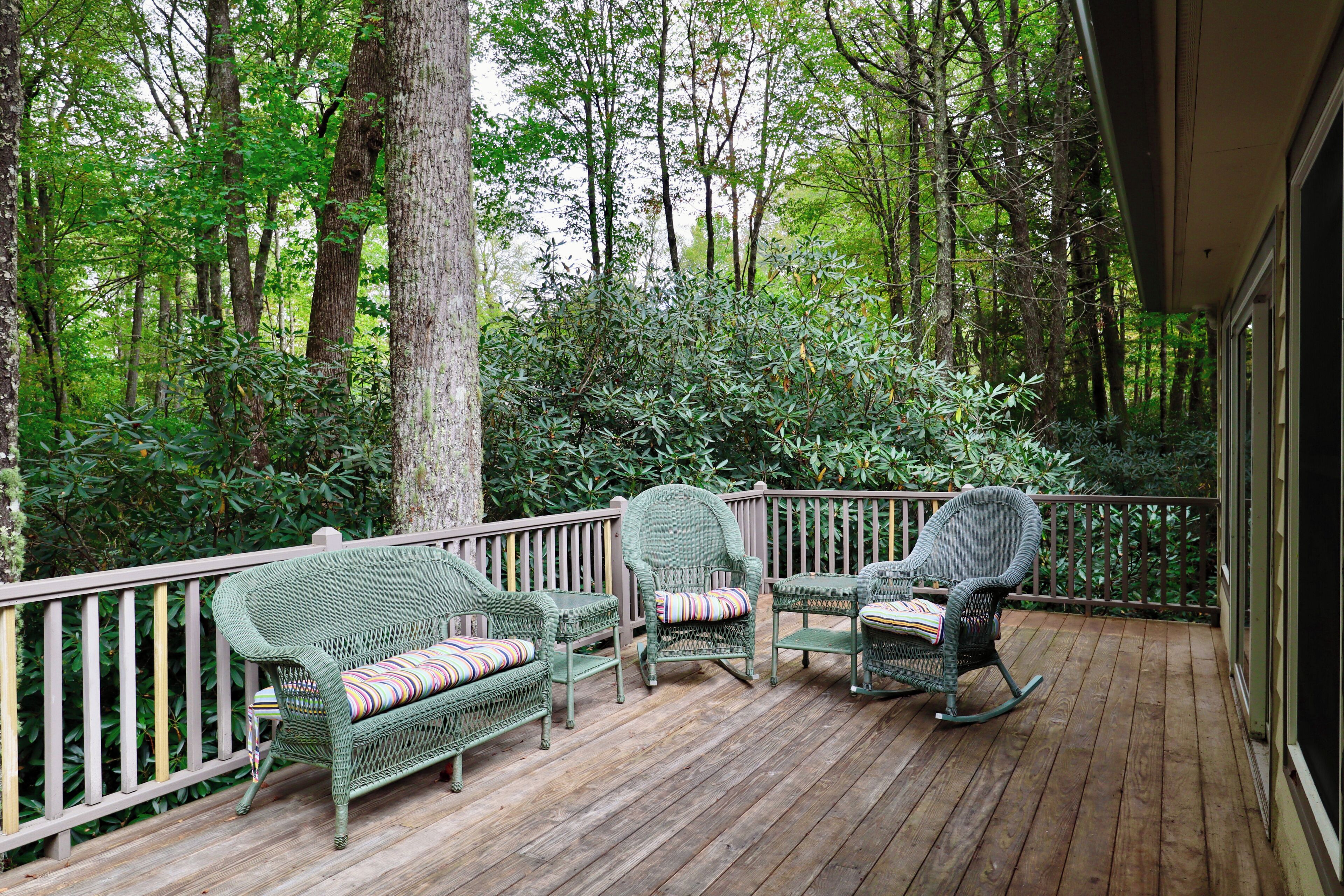Une terrasse en bois, dotée de meubles en osier et d’une rambarde.