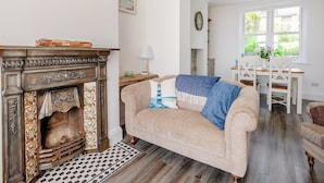 A living room with a fireplace, a sofa, a dining table with chairs, and a view of greenery outside. - Stunning views of the English Channel and Brighton Marina. (Brighton)