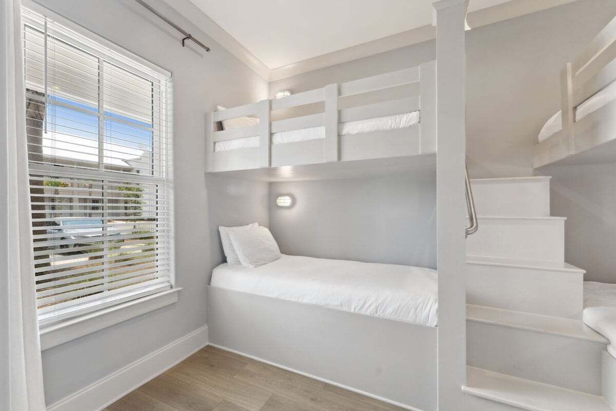 A bedroom with a bunk bed, a window with blinds, a staircase, and a wall-mounted light fixture.