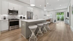 Une cuisine moderne avec des meubles blancs, des appareils en acier inoxydable et un îlot central doté de tabourets de bar.