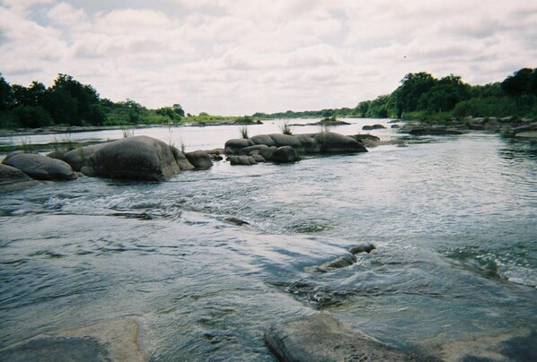 Une rivière avec de gros rochers au milieu et une zone boisée en arrière-plan.