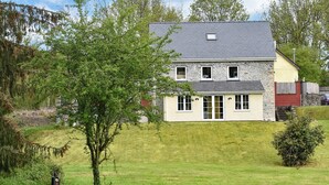 Une maison à deux étages, dotée d’une façade en pierre, de nombreuses fenêtres et d’un toit en pente.