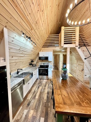 A modern kitchen with wooden walls, a wooden staircase, and a dining area.