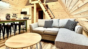 L’intérieur chaleureux d’un chalet avec un plafond en bois, un canapé, une table à manger et un escalier.