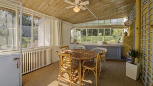 Une pièce baignée de lumière, avec un plafond en bois, une table à manger entourée de chaises, un radiateur et une horloge au mur.