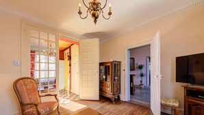 Un salon avec un plancher en bois, une table basse en bois, un fauteuil à motifs floraux, un téléviseur et un meuble.