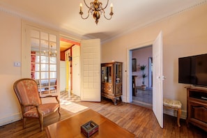 Un salon avec un plancher en bois, une table basse en bois, un fauteuil à motifs floraux, un téléviseur et un meuble.