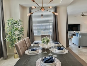 Een eetgedeelte met een tafel voor vier personen, een potplant en een moderne plafondlamp.