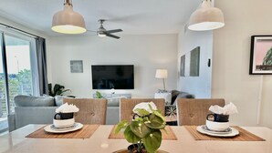 Ein modernes Wohnzimmer mit Esstisch, zwei Stühlen, einer Couch, einem Fernseher und einem Deckenventilator.