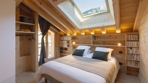 Ein gemütliches Schlafzimmer aus Holz mit Dachfenster, einem großen Bett, eingebauten Bücherregalen und Blick ins Freie.
