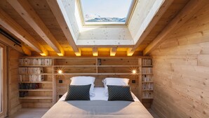 Ein gemütliches Zimmer mit Dachfenster, hölzernen Bücherregalen, einem Bett mit Kissen und Blick auf die Berge.