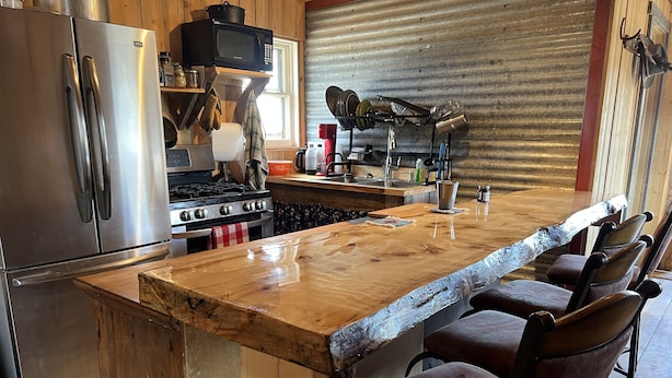 Een keuken met een houten eiland, roestvrijstalen apparatuur en barstoelen.