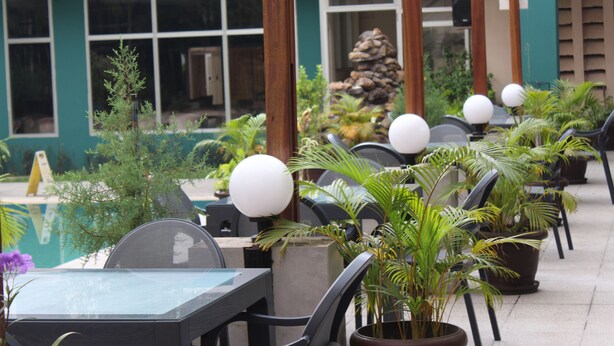 An outdoor seating area with tables and chairs, surrounded by potted plants and a stone wall. - Hotel Belle Vie (Kinshasa)
