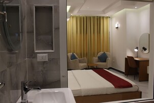 Una habitación de hotel con una cama grande, un escritorio, dos sillas, un espejo y un baño con bañera y ducha.