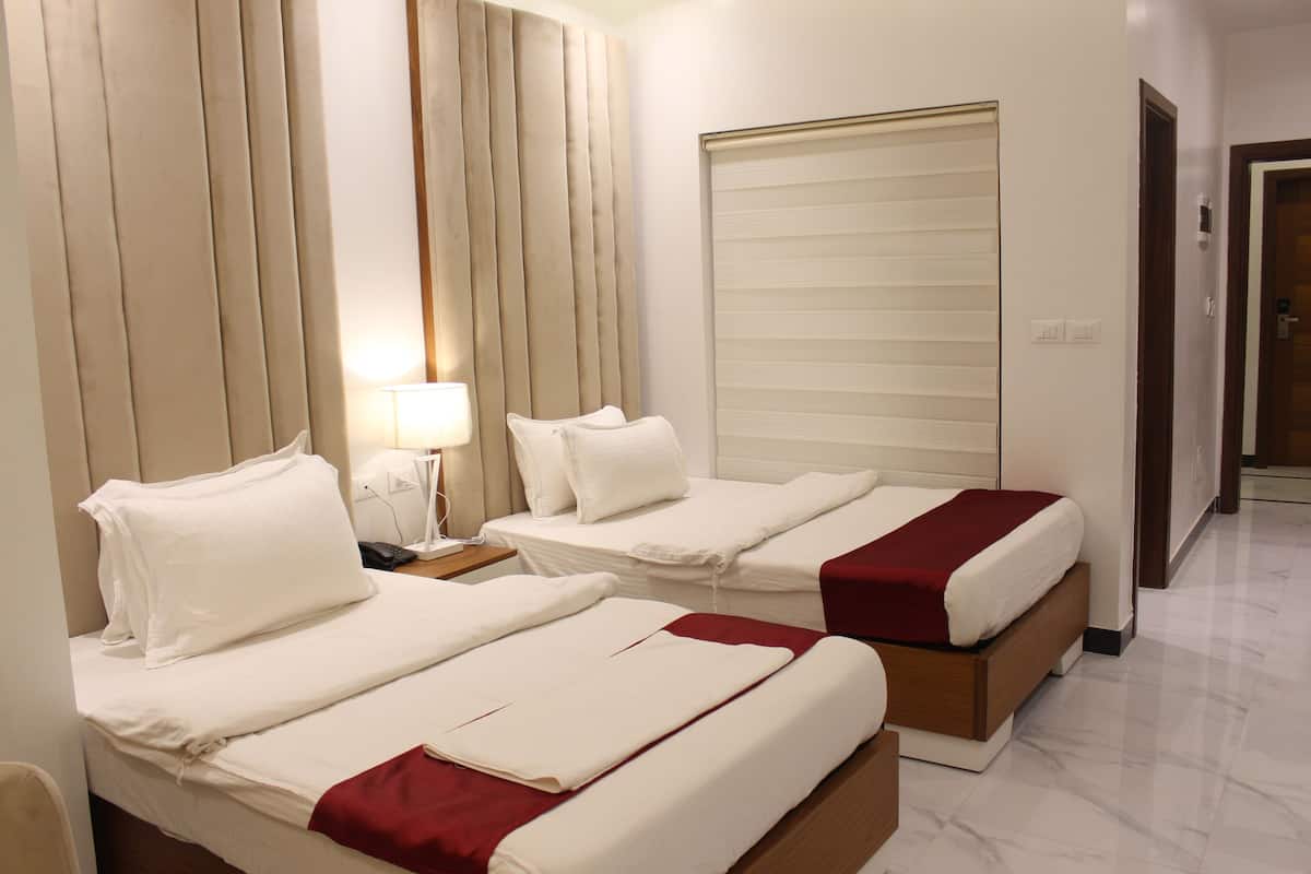 Habitación de hotel con dos camas, una mesita de noche con lámpara y un ventanal con persianas.