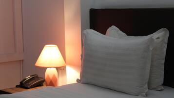 A neatly made bed with white pillows and a dark headboard, a bedside lamp, and a telephone on a wooden nightstand.