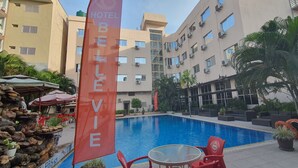 A hotel pool area with a large pool, red chairs, and a 'BELIEVE' banner. - Hotel Belle Vie (Kinshasa)