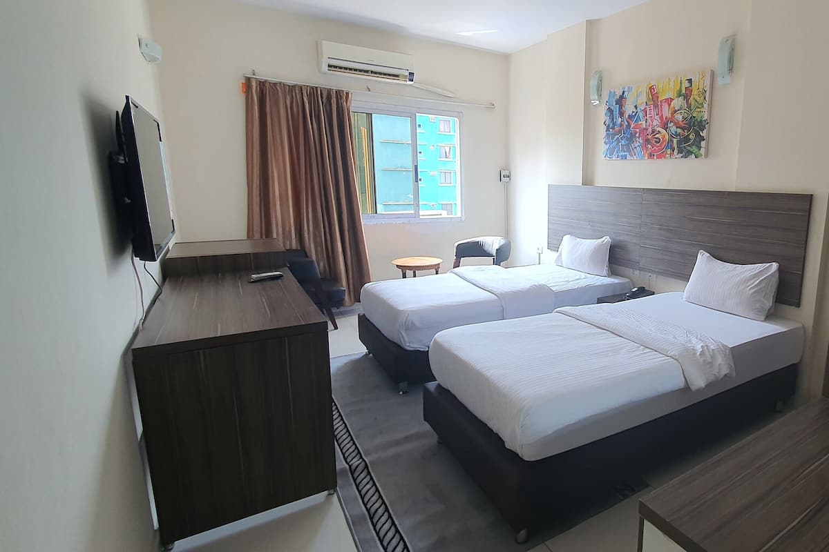 Habitación de hotel con dos camas, un escritorio, una silla, un televisor y una ventana con cortinas.