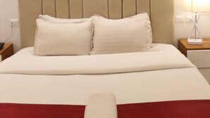 A neatly made bed with white linens and a red accent, a wooden headboard, and a bedside lamp. - Hotel Belle Vie (Kinshasa)