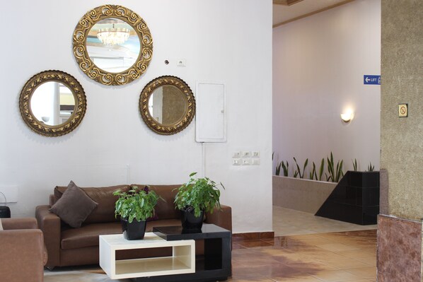 Un espace d’accueil avec un canapé en cuir marron, deux plantes en pot et trois miroirs décoratifs accrochés au mur.