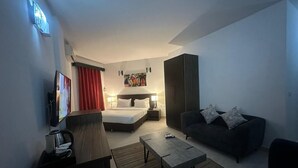 A hotel room with a bed, a sofa, a coffee table, a TV, and artwork on the wall. - Hotel Belle Vie (Kinshasa)