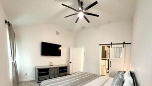 Ein Schlafzimmer mit einem Bett, einem Deckenventilator, einem Fernseher, einem Kleiderschrank und einer Tür zu einem anderen Raum.