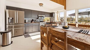 A modern kitchen with stainless steel appliances, a dining area with a wooden table and chairs, and large windows offering a view of the outdoors. - Waterfront | Minutes to US Open| Private Water Access (Hampton Bays)