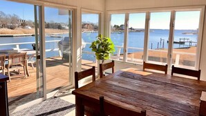 A dining area with a wooden table and chairs, large sliding glass doors leading to a deck with a view of a body of water. - Waterfront | Minutes to US Open| Private Water Access (Hampton Bays)
