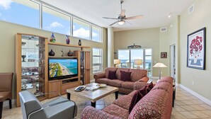A spacious living room with a large flat-screen TV, comfortable seating, and a balcony with a view of the ocean. - Beautiful Gulf View, Private Beach Access, Fitness Room (Siesta Key)