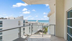 A balcony with a view of the beach and ocean, white buildings, and a clear sky.