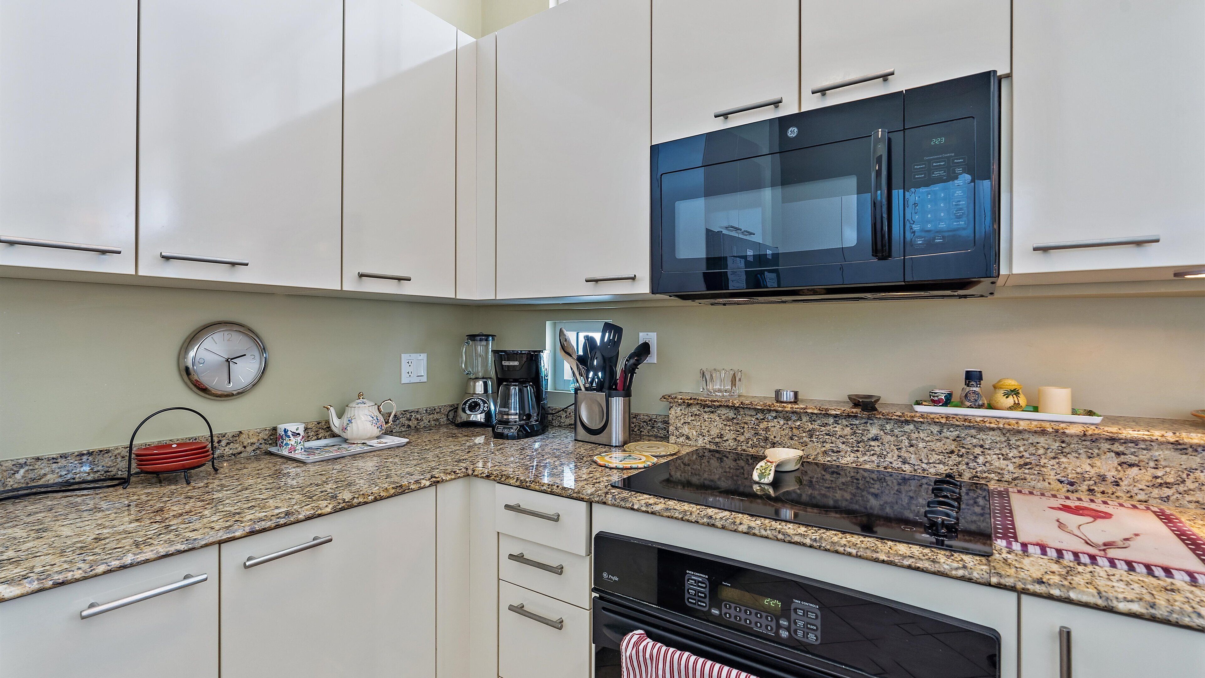 A modern kitchen with white cabinets, a granite countertop, a microwave, a coffee maker, and a clock.